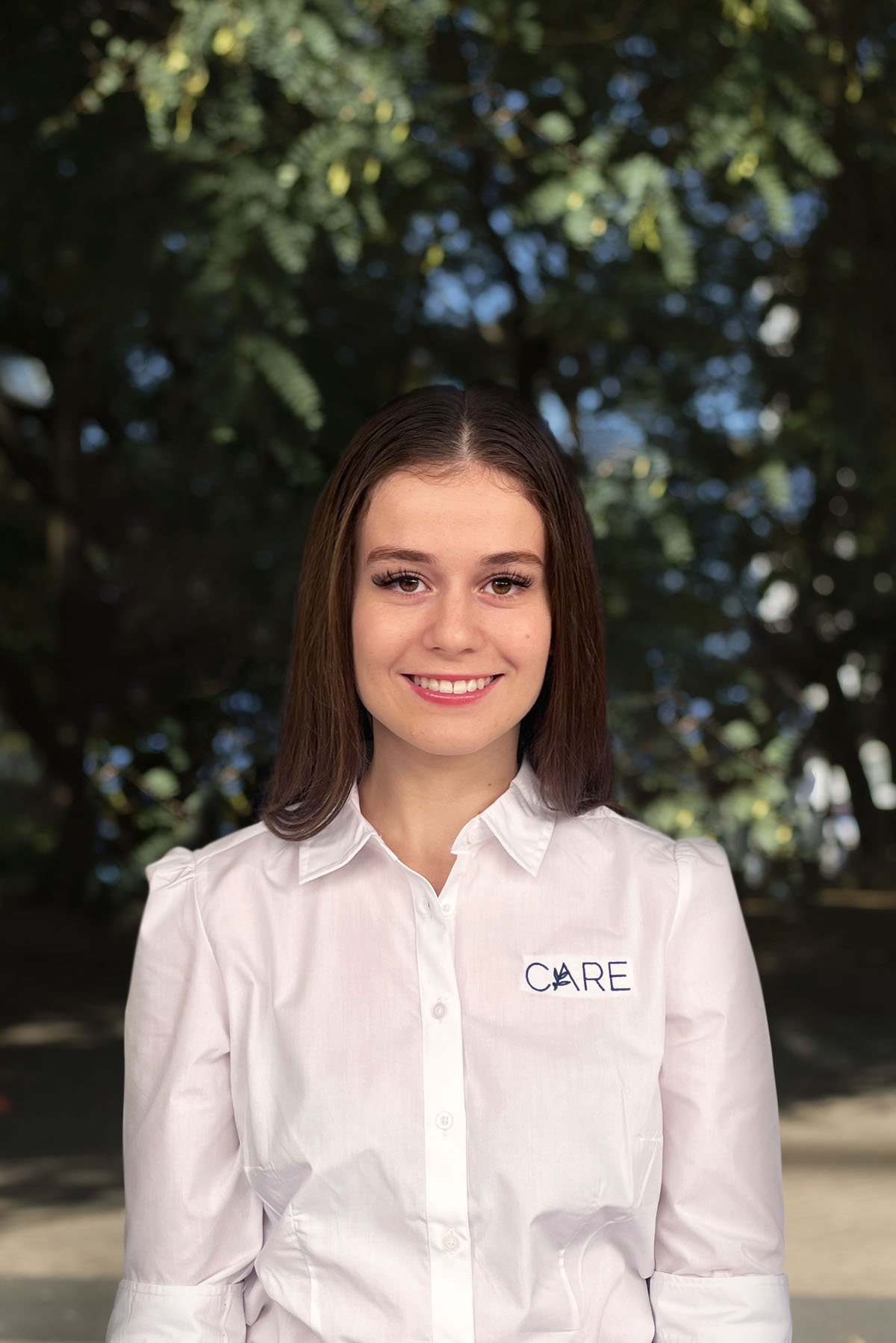 A young woman in a white shirt is smiling.