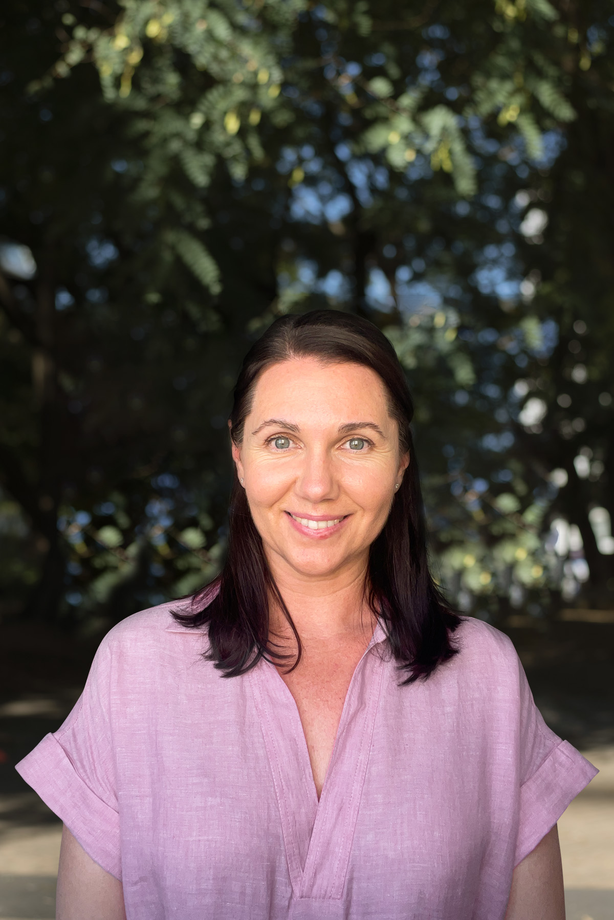 A woman in a pink shirt standing in front of trees.